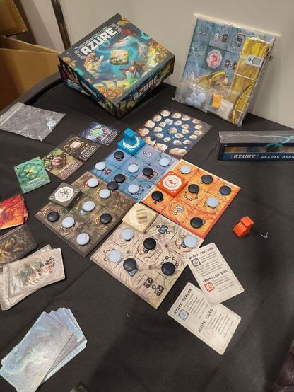 Schräg von oben fotografiertes Spiel „Azure“, bei dem vier quadratische Plättchen in unterschiedlichen Farben mit 3×3 Feldern einen Spielplan von 6×6 Feldern ergeben. Auf den Feldern befinden sich unterschiedliche Symbole, viele sind mit runden Spielsteinen in Weiß oder Schwarz belegt. Am Rand liegen ein paar Karten. Hinten liegt der Spielekarton, auf dem sich unter dem Schriftzug ein springender Tiger und ein fliegender Vogel gegenüber„stehen“.