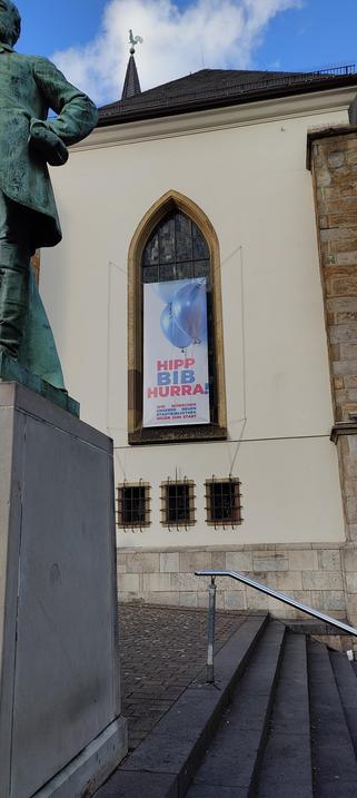 Werbebanner an einer Kirche neben der neuen Bib, auf der steht Hipp, Bib, Hurra