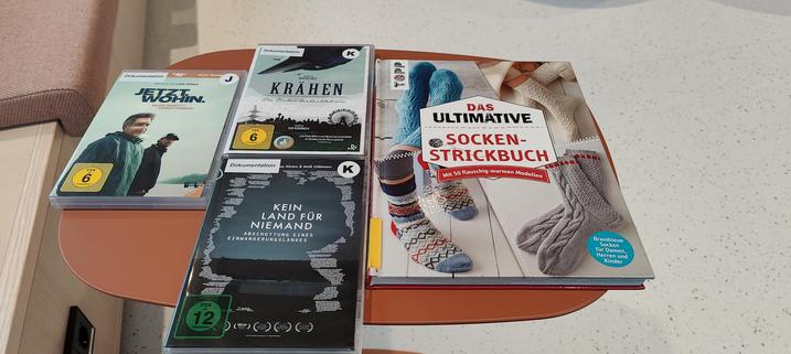 Drei DVD Titel und ein Strickbuch liegen auf einem kleinen Tisch.
Die Titel der Filme sind
Jetzt. Wohin.
Krähen 
Kein Land für niemand